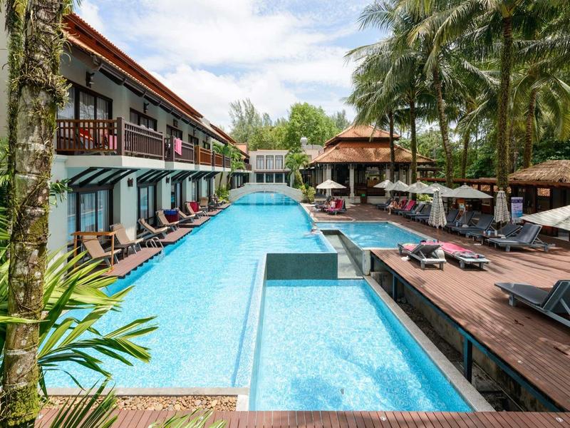 Großer blauer Pool mit Liegestühlen, Palmen und Hotelgebäude bei sonnigem Himmel.
