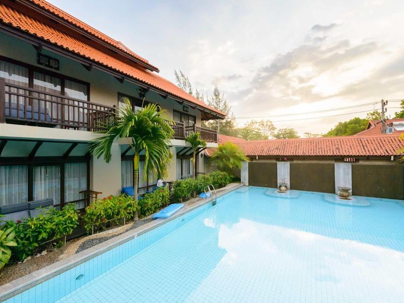 Moderner Außenpool neben zweistöckigem Haus mit Balkon, Palmen und bewölktem Himmel.
