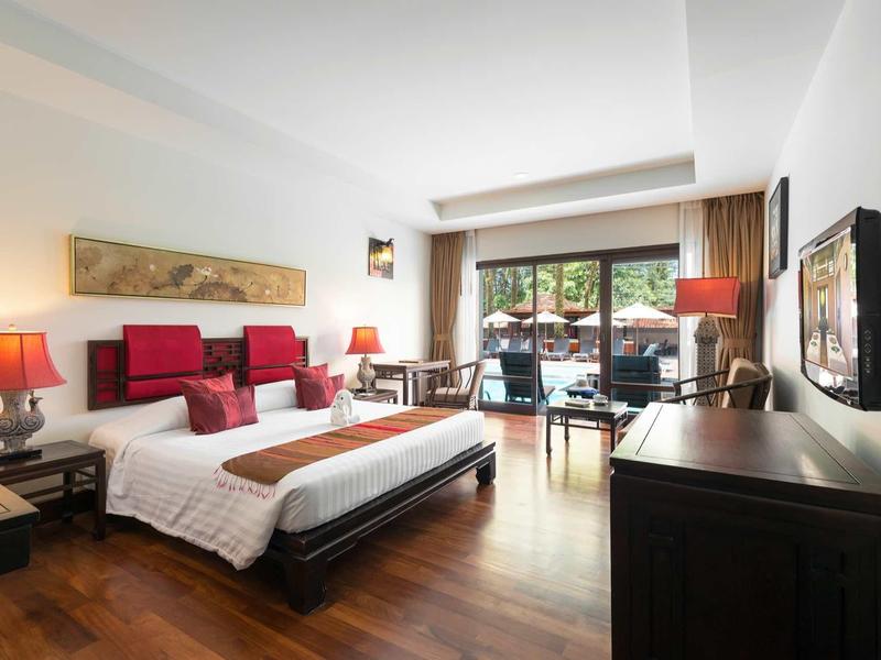 Großes Schlafzimmer mit Doppelbett, Holzboden, roten Akzenten und Balkon mit Gartenblick.