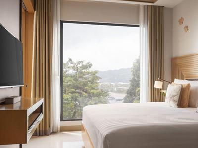 Camera d'hotel moderna con letto grande, TV a parete e vista su alberi e montagne.