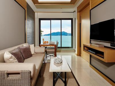 Camera d'albergo moderna con divano, TV e vista sul mare attraverso grandi finestre.