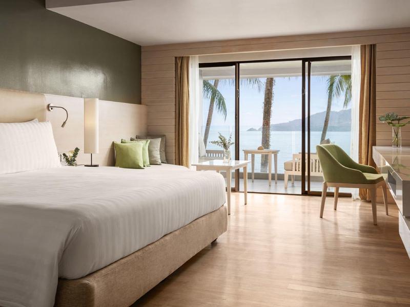 Camera d'hotel luminosa con letto grande, area salotto e balcone con vista mare.