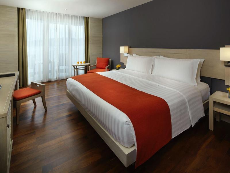 Camera d'hotel moderna con letto grande, pavimento in legno e zona salotto vicino alla finestra.