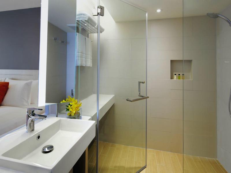 Bagno moderno con doccia a filo pavimento, lavabo e vista sulla camera da letto.