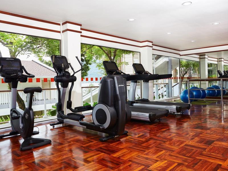 Palestra luminosa con tapis roulant e biciclette davanti a grandi finestre con vista sugli alberi.