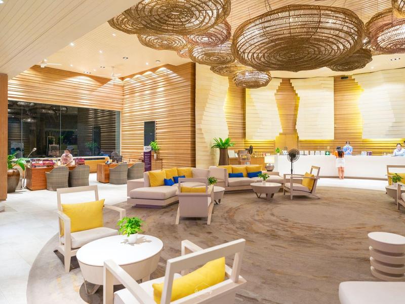 Luminosa hall dell'hotel con arredi moderni, pavimento moquettato e luci decorative sul soffitto.