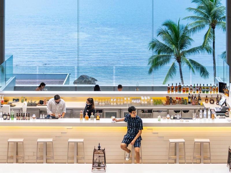 Bar dell'hotel moderna con posti a sedere e vista mare dietro parete di vetro.