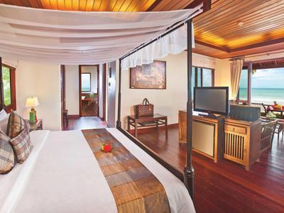 Elegante habitación de hotel con cama con dosel, muebles de madera y vista al mar a través de grandes ventanas.