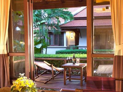 Blick durch ein offenes Fenster auf Garten mit Stühlen und Tisch vor einem Hotelgebäude.