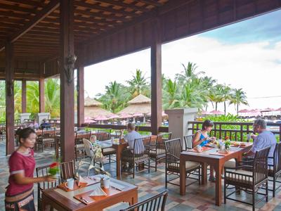 Restaurante abierto con techo de madera, mesas con clientes y vista de plantas tropicales