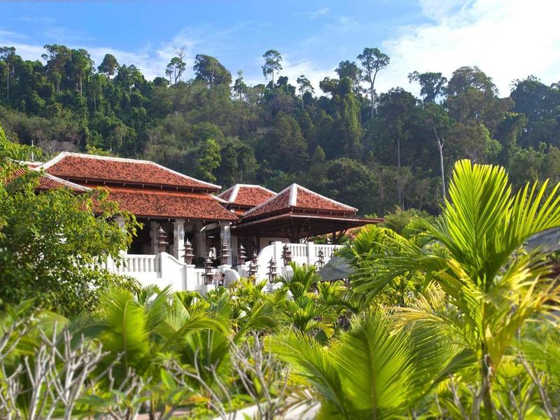 Ein weißes Haus mit rotem Dach umgeben von grünem tropischem Wald und Sträuchern.