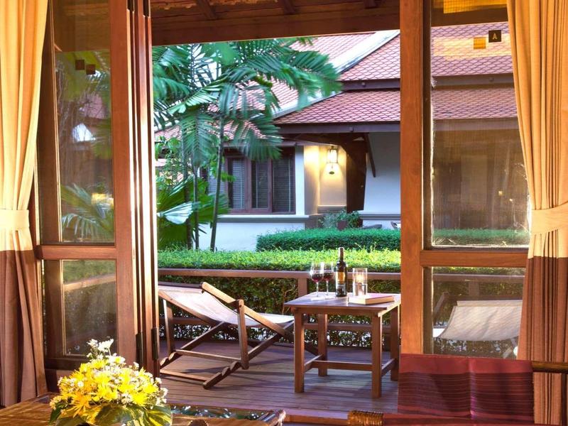 Blick durch ein offenes Fenster auf Garten mit Stühlen und Tisch vor einem Hotelgebäude.