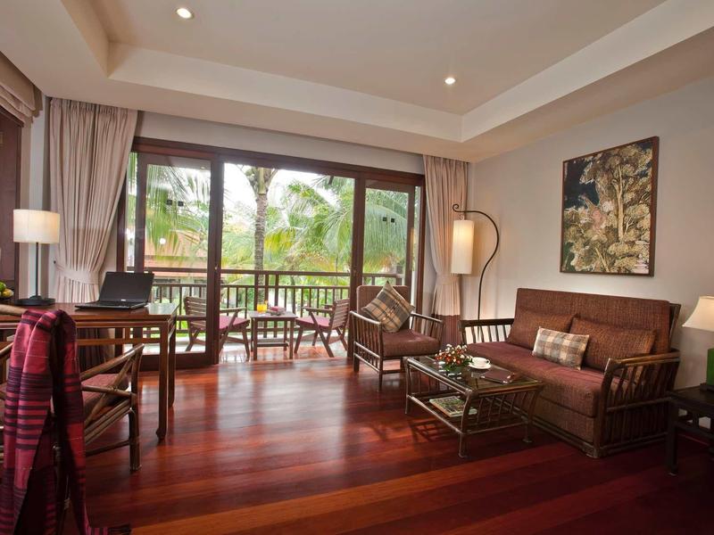 Helles Wohnzimmer mit Holzboden, Sofa, Sesseln, Lampen und großem Fenster mit Blick auf die Natur.