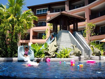 Hôtel de luxe en bord de mer avec plusieurs bâtiments, piscine et jardin tropical sous un ciel bleu.