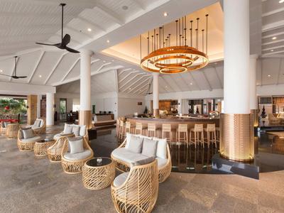 Hall d'hôtel moderne et lumineuse avec des fauteuils en rotin et un grand bar en arrière-plan.