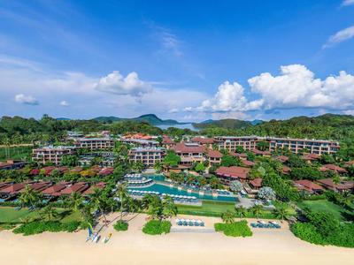 Großes Resort mit Pool, umgeben von viel Grün, vor einem weißen Sandstrand und blauem Himmel.