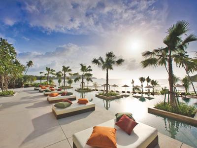 Espace piscine luxueux avec transats et palmiers sous un ciel matinal nuageux.