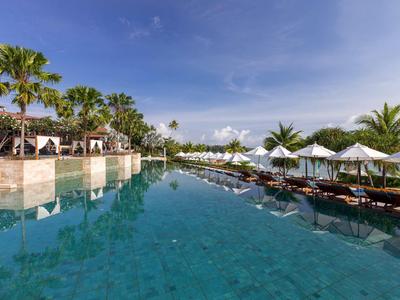 Grande piscine avec chaises longues et parasols dans un hôtel tropical.