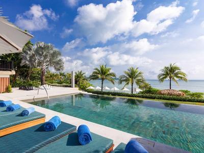 Pool mit blauen Handtüchern und Palmen am Meer unter blauem Himmel mit Wolken