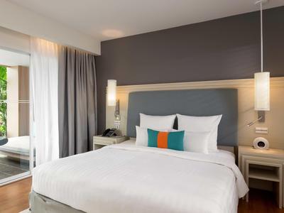 Chambre d'hôtel moderne avec grand lit, tables de chevet et vue sur une terrasse avec jardin.