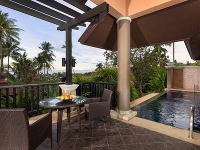 Balcon avec table, chaises, piscine et palmiers dans un hôtel tropical.