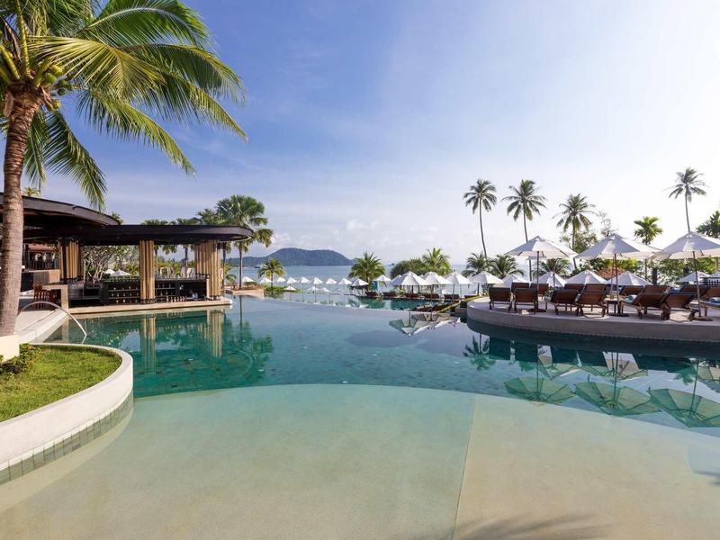 Infinity zwembad met uitzicht op zee, omgeven door palmbomen en ligstoelen onder een blauwe lucht.