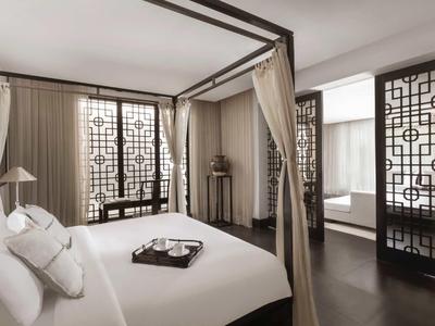 Camera elegante con letto a baldacchino, pannelli decorativi alle finestre e pavimento in legno scuro in hotel.