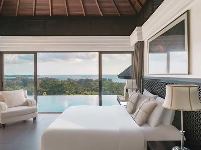 Camera moderna con grande letto, poltrone e finestre panoramiche con vista sul mare.