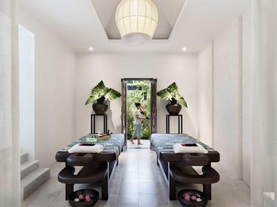 Stanza spa minimalista con lettini da massaggio e piante vicino a una porta aperta.