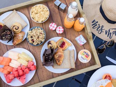 Vassoio per la colazione con frutta fresca, dolci, succhi e granola accanto a un cappello di paglia