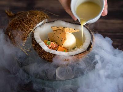 Dessert esotico in una noce di cocco divisa a metà con salsa e effetto fumo.