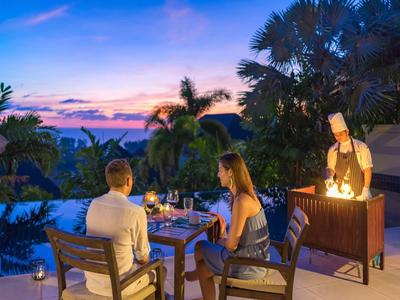 Coppia che gode di una cena romantica all'aperto vicino a una piscina tropicale con chef al tramonto.
