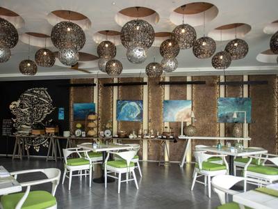 Sala da pranzo moderna con sedie bianche e cuscini verdi sotto luci a soffitto sferiche.