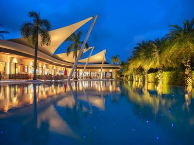 Piscina moderna dell'hotel con palme e tetti a vela illuminati di notte.