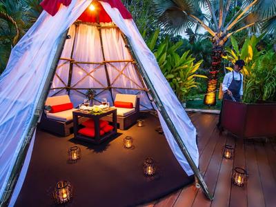 Accogliente lounge in tenda con cuscini, lanterne e ambiente tropicale notturno.