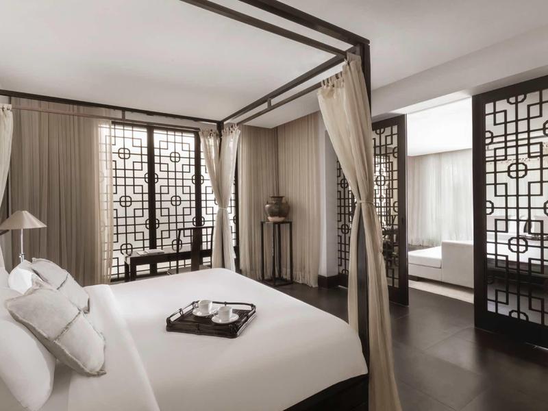 Camera elegante con letto a baldacchino, pannelli decorativi alle finestre e pavimento in legno scuro in hotel.