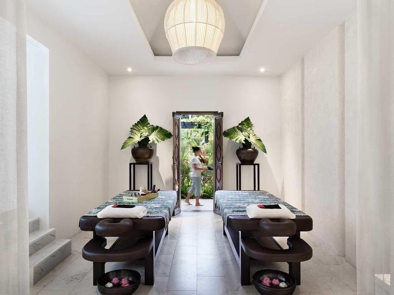 Stanza spa minimalista con lettini da massaggio e piante vicino a una porta aperta.
