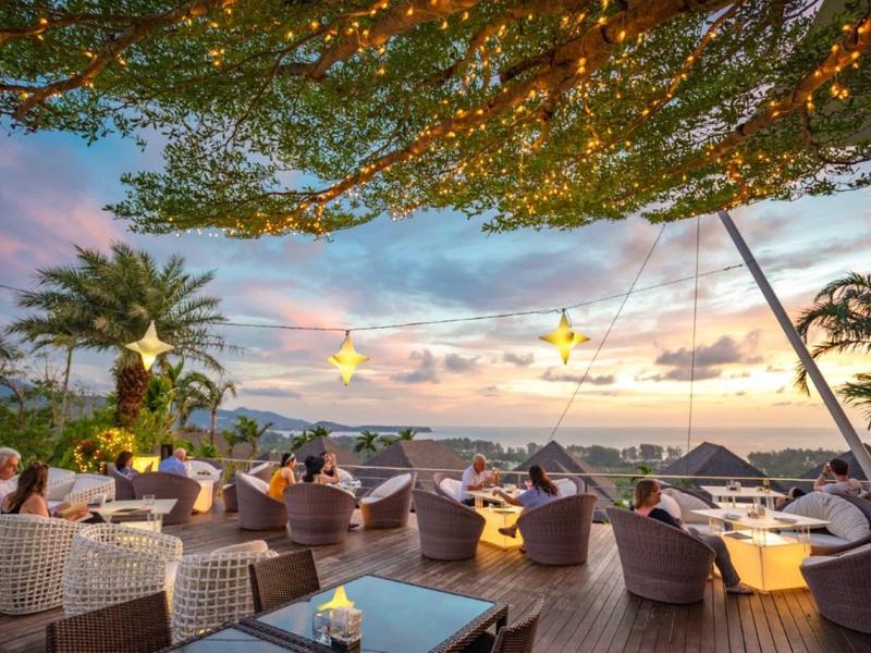 Terrazza esterna con posti a sedere, illuminazione e vista mare al tramonto.