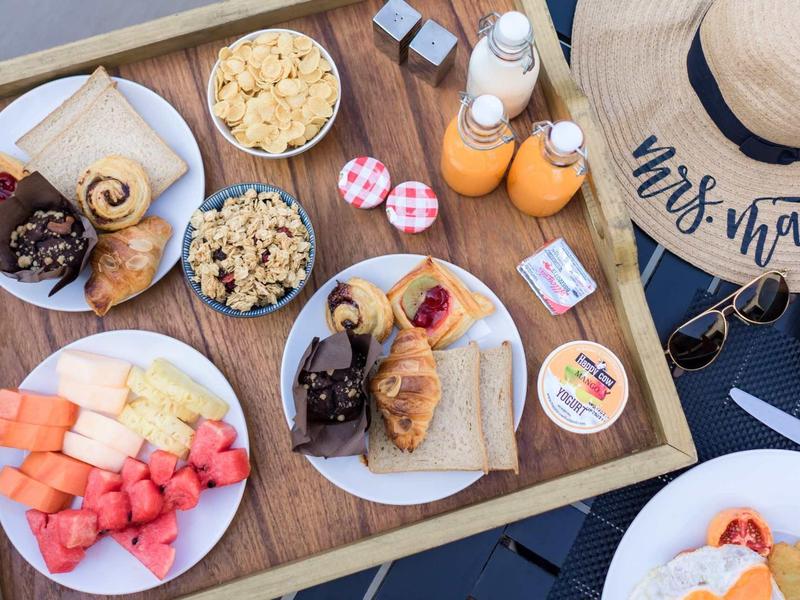 Vassoio per la colazione con frutta fresca, dolci, succhi e granola accanto a un cappello di paglia