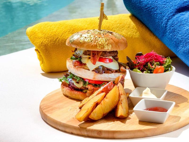 Burger con patatine e insalata su tagliere di legno vicino alla piscina con asciugamani colorati