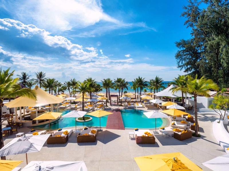 Grande piscina con lettini e ombrelloni in un resort tropicale sotto un cielo azzurro