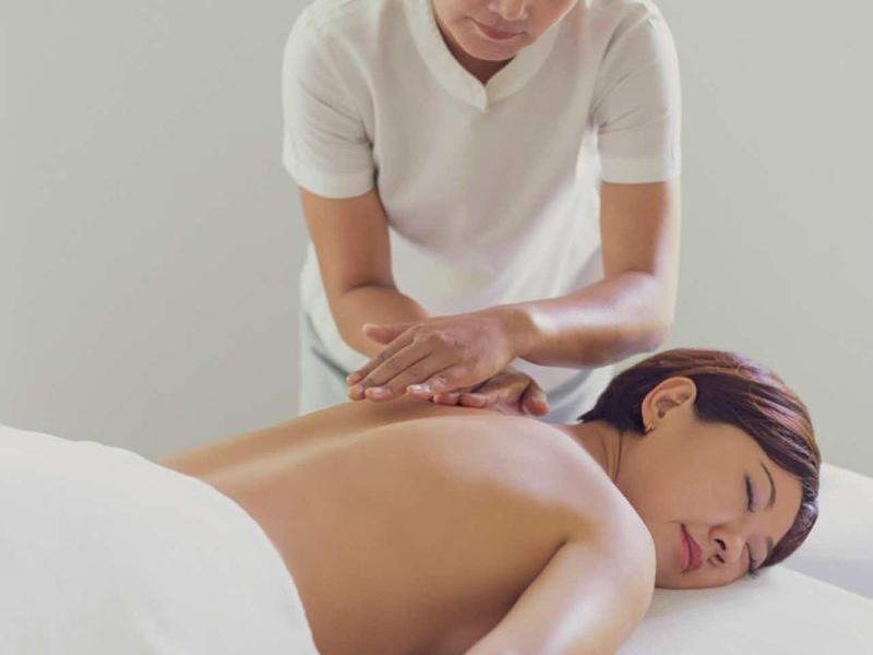 Donna che riceve un massaggio alla schiena in una stanza tranquilla e arredata di bianco.