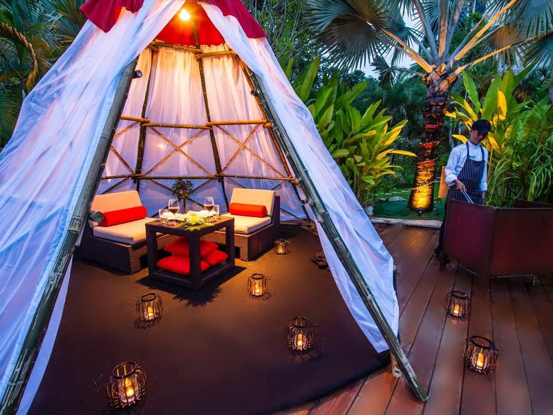 Accogliente lounge in tenda con cuscini, lanterne e ambiente tropicale notturno.