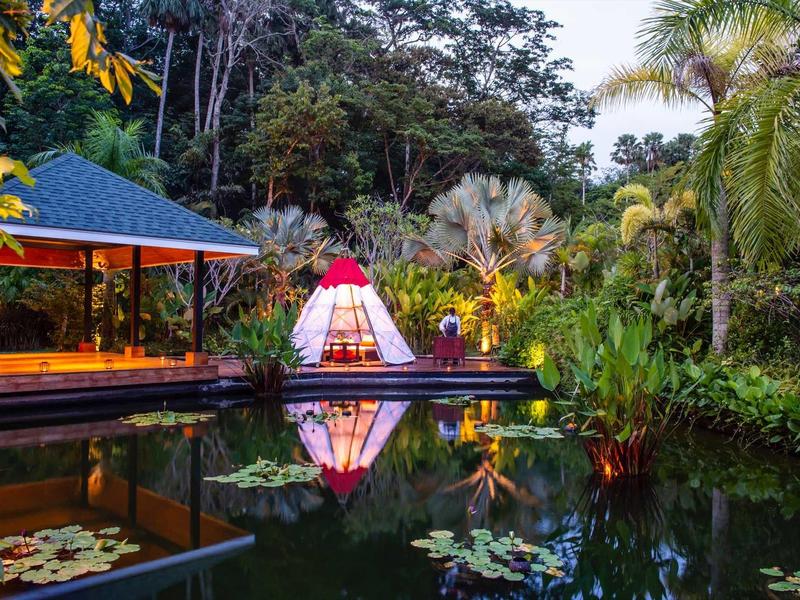 Uno stagno tranquillo al tramonto accanto a un padiglione boscoso con illuminazione a tenda.