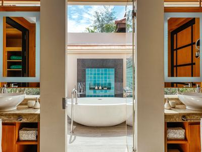 Baño lujoso con bañera independiente junto a pared de vidrio y dos lavabos con espejos.