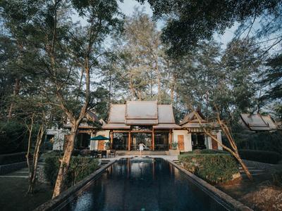 Ein großes Haus mit Holzfassade umgeben von Bäumen und einem langen, schmalen Pool im Vordergrund.