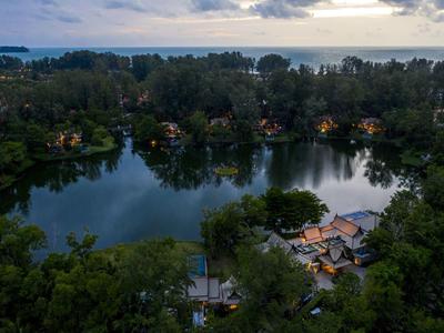 Runder See mit Häusern und vielen Bäumen, dahinter Meer unter bewölktem Himmel bei Dämmerung.