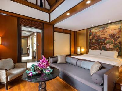 Habitación de hotel elegante con muebles de madera, cama acogedora y área de estar con mesa y flores.