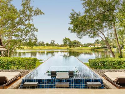 Piscina infinita moderna con vista a un lago rodeado de árboles.