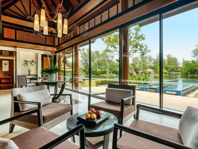 Área de salón luminosa con techo de vigas de madera, sillones modernos y vista a la piscina y el jardín.